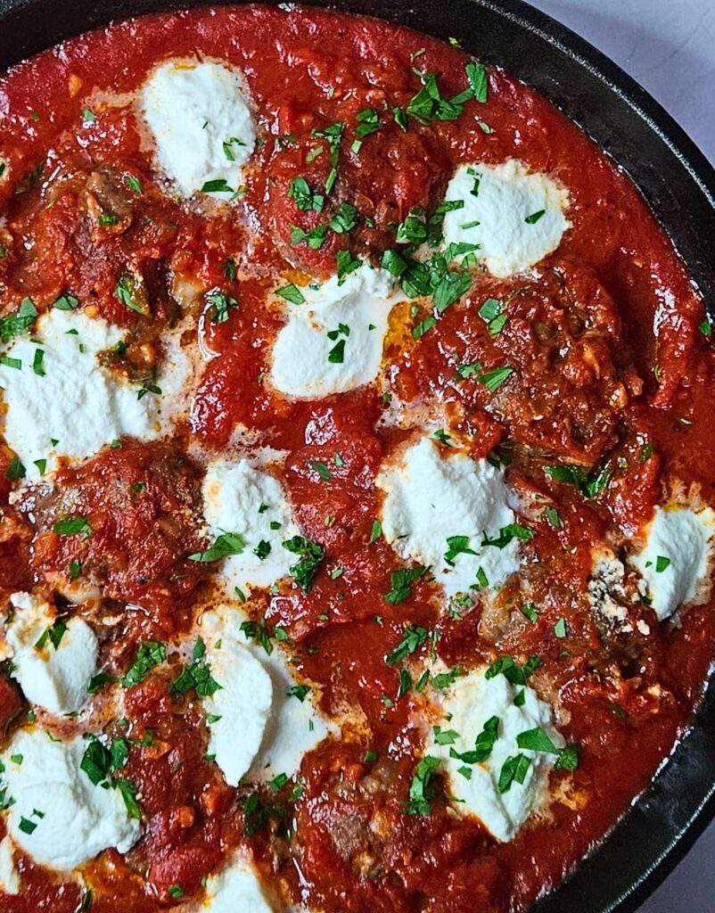 Ricotta meatballs in homemade marinara sauce in a cast iron skillet with dollops or ricotta cheese on top.