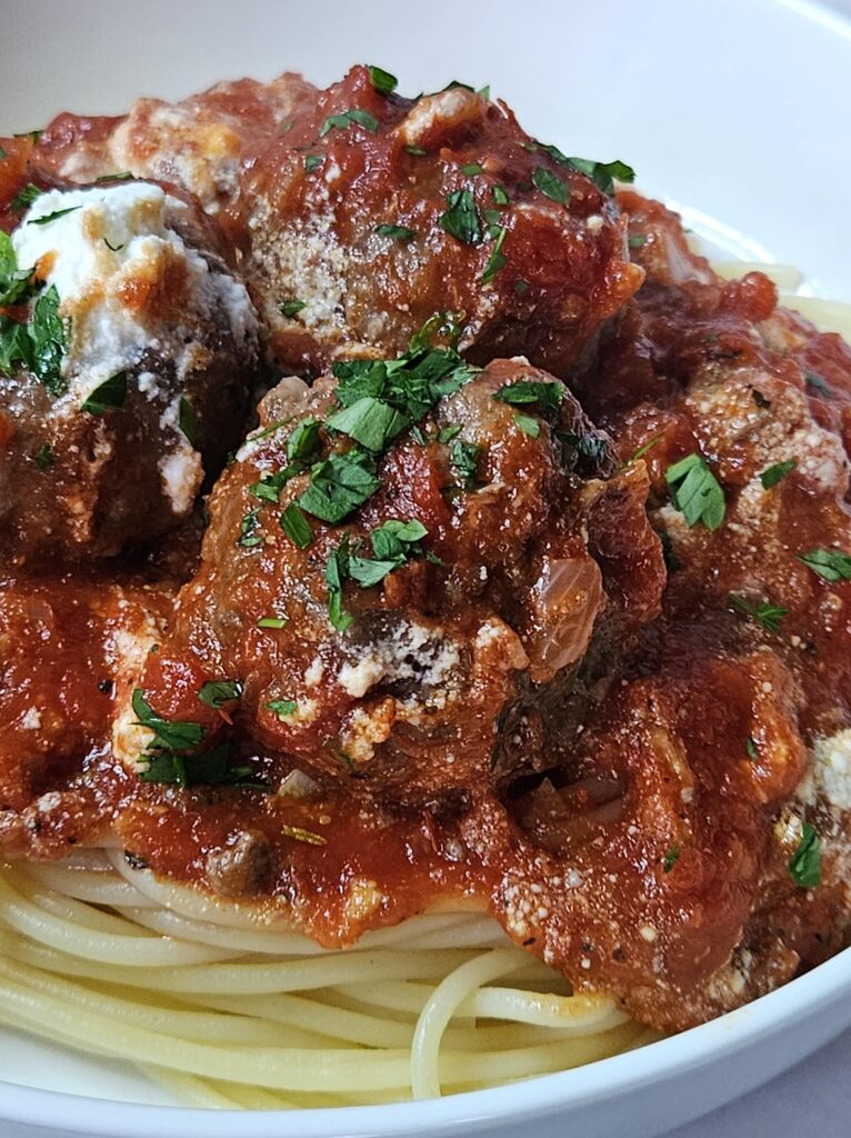 Ricotta meatballs with homemade marinara sauce being served over spaghetti pasta.