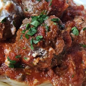 Close up image of ricotta meatballs with homemade marinara sauce being served over spaghetti pasta.