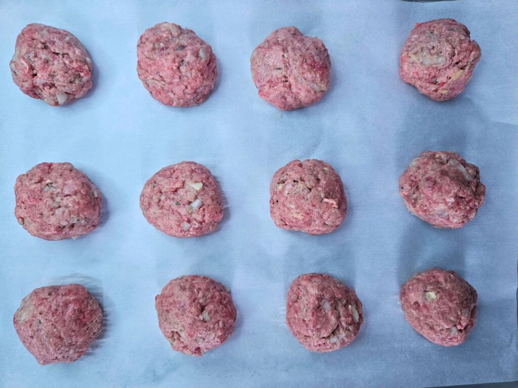 Ricotta meatballs rolled and on a sheet pan before baking in the oven.