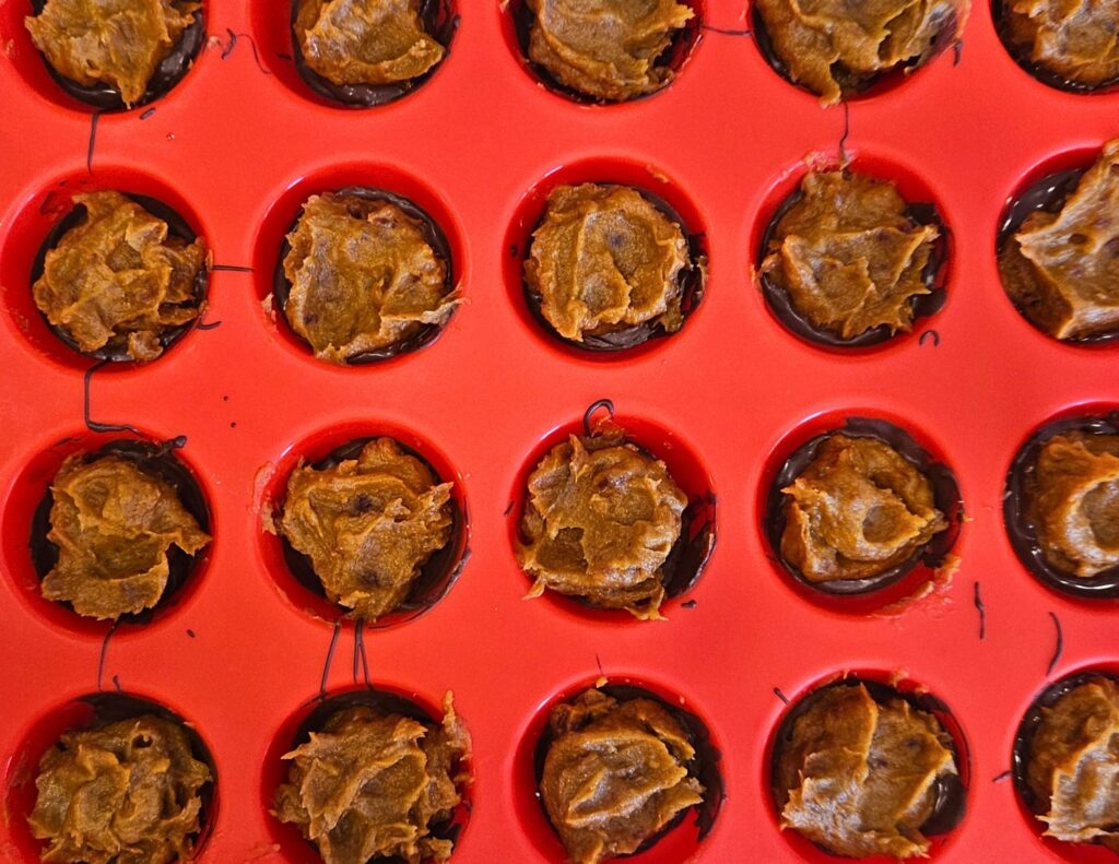 Assembling the pumpkin caramel over the dark chocolate in a silicone muffin pan.