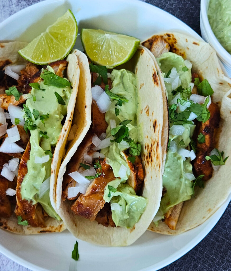 Maple Chipotle Chicken Tacos 5 Image of maple chipotle chicken tacos being served with avocado crema and limes.