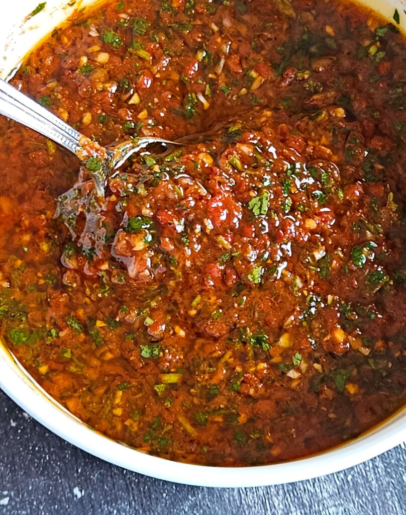 Image of red chimichurri being served in a white bowl.