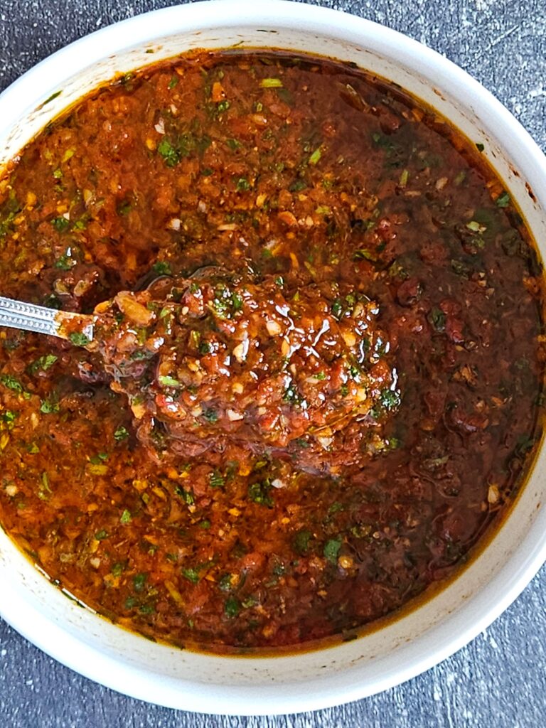Image of red chimichurri sauce being scooped with spoon.