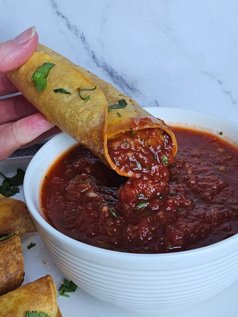Image of cream cheese taquitos being dipped into salsa.
