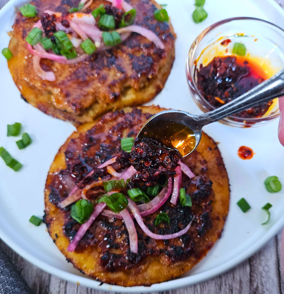 Image of sticky ground chicken smashed dumpling tacos being served with pickled onions, green onions and chili crisp.