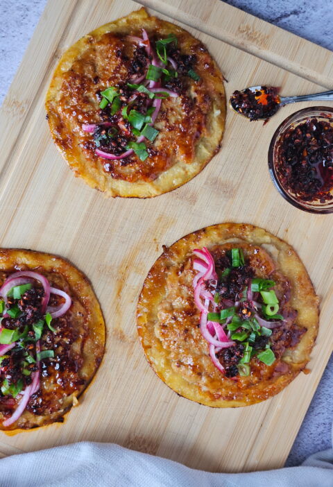 Image of ground chicken smashed dumpling tacos on a wooden cutting board with chili crisp.