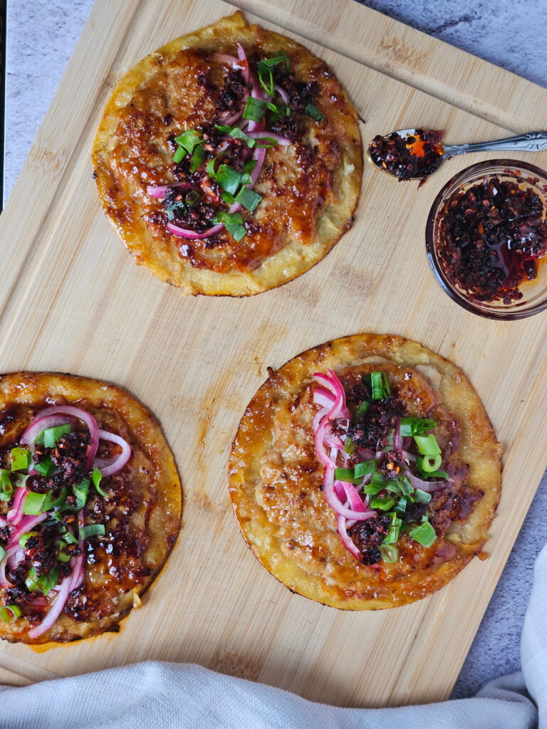 Image of ground chicken smashed dumpling tacos on a wooden cutting board with chili crisp.