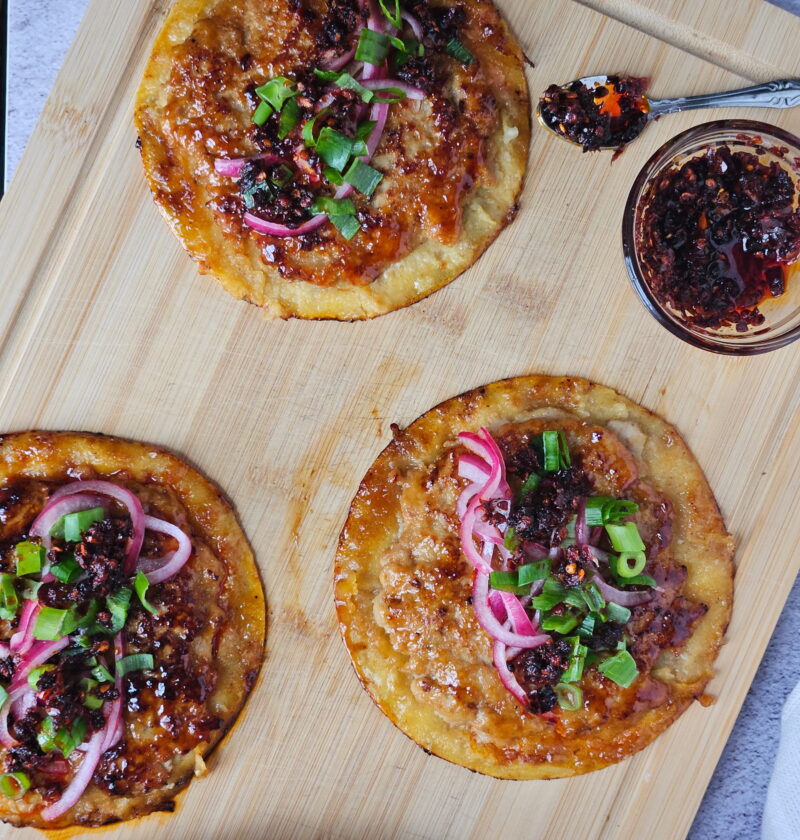 Image of ground chicken smashed dumpling tacos on a wooden cutting board with chili crisp.