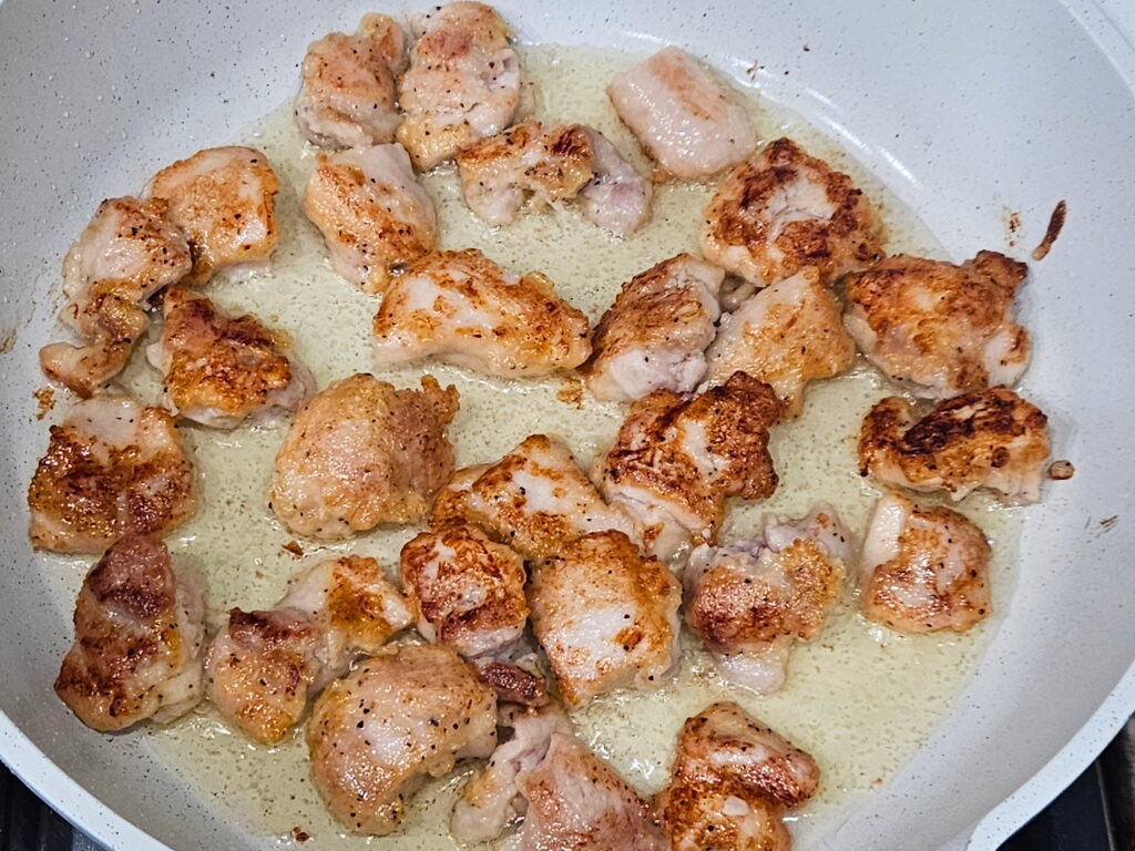 Image of chicken pieces being seared in a skillet. 