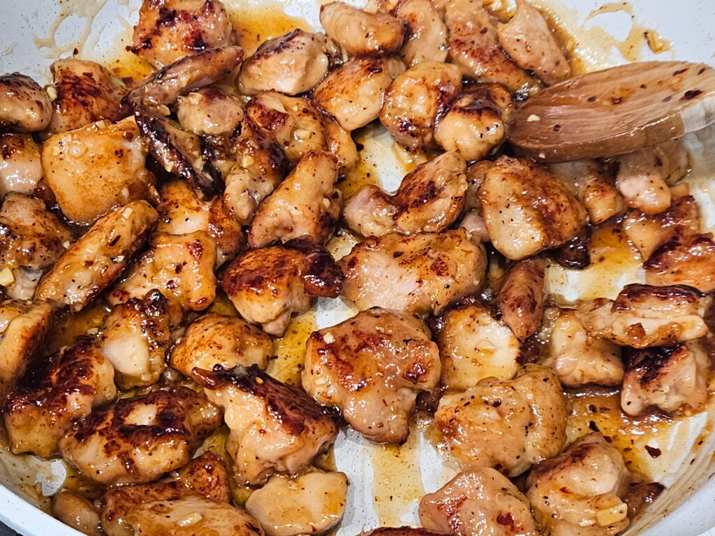 Image of honey ginger chicken pieces being tossed in the honey ginger sauce. 